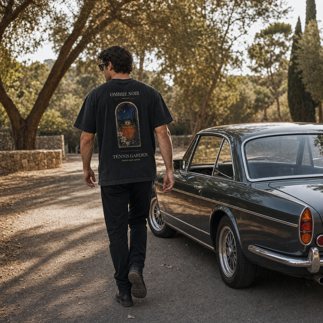 Back of black Tennis Garden T-Shirt worn outdoors beside a dark classic car