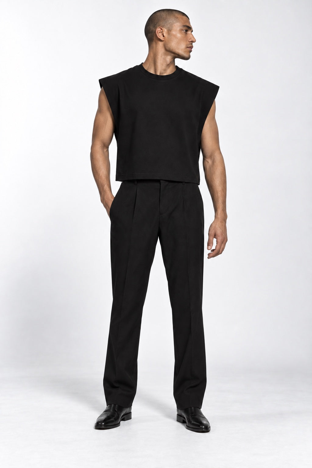 Full-body buzzcut male model wearing the black Contour Cropped Tank, standing naturally and looking right in a white studio