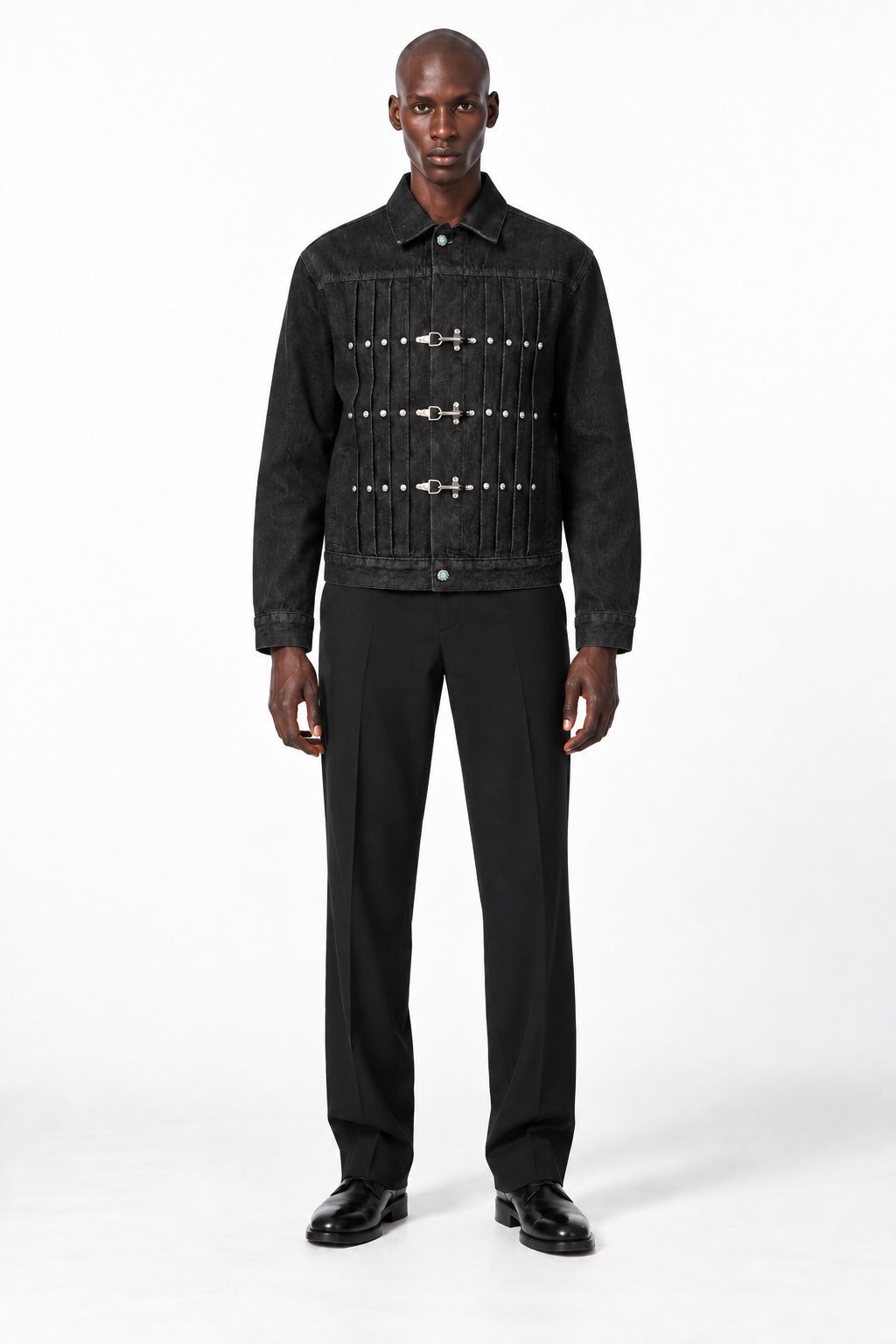 Full-body shaved-head male model wearing the black Latch Buckle Denim Jacket, looking directly at the camera in a white studio