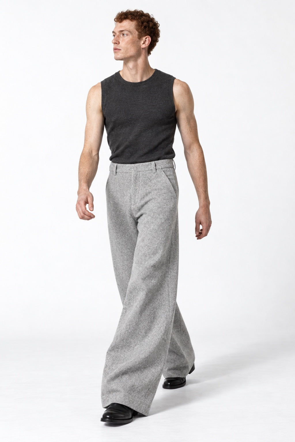 Full-body copper-haired male model walking in light-grey Traverse trousers, looking left in a white studio